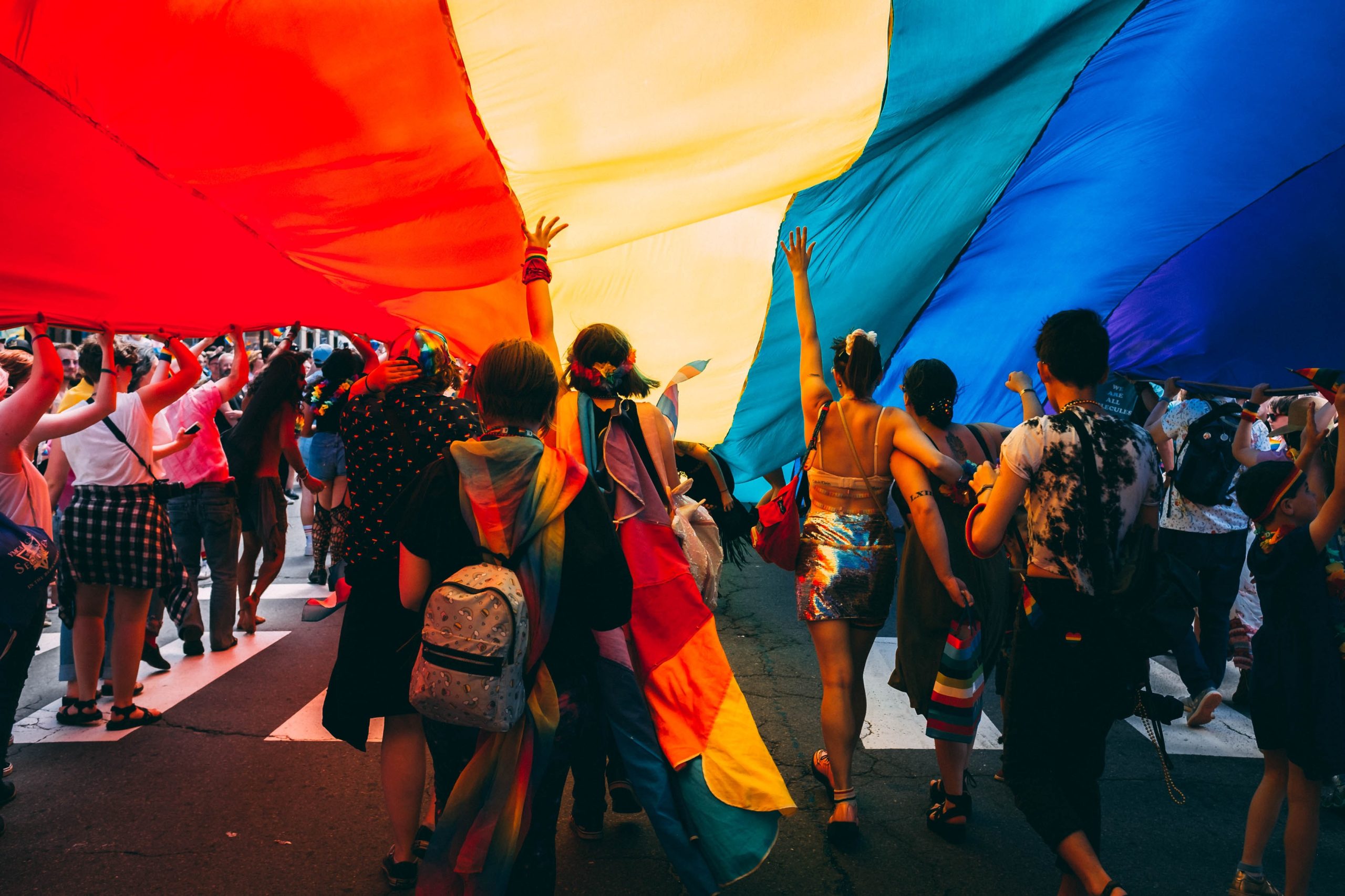 Menschen mit großer Regenbogenflagge über sich.